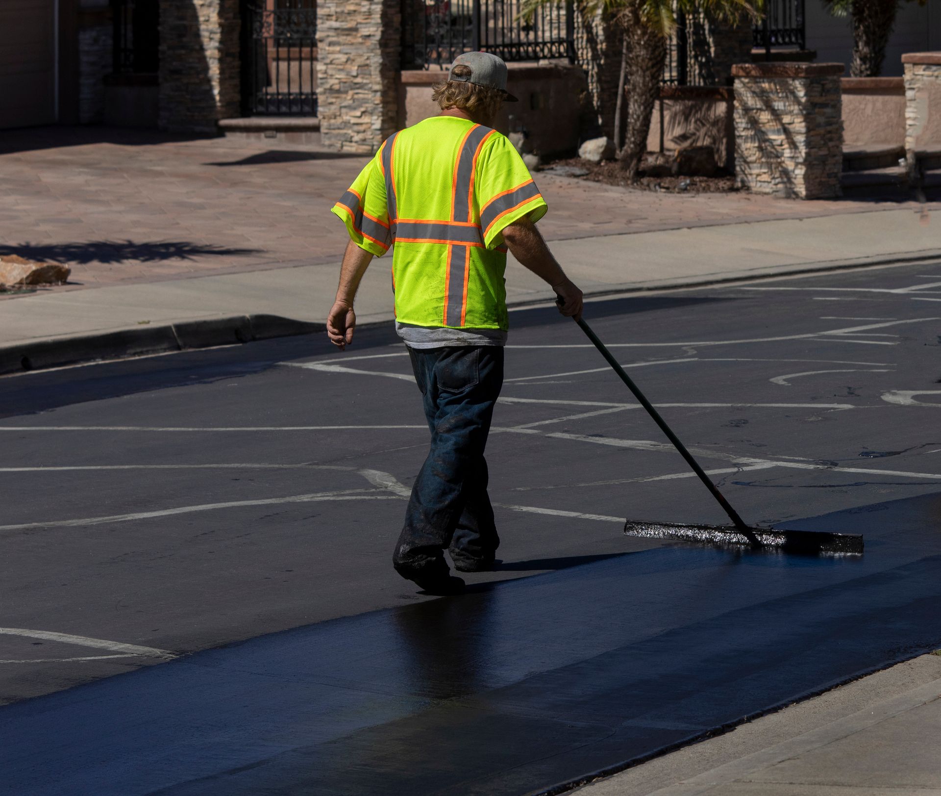 A worker is applying a protective layer of asphalt sealcoating. A worker is applying a protective layer of asphalt sealcoating.