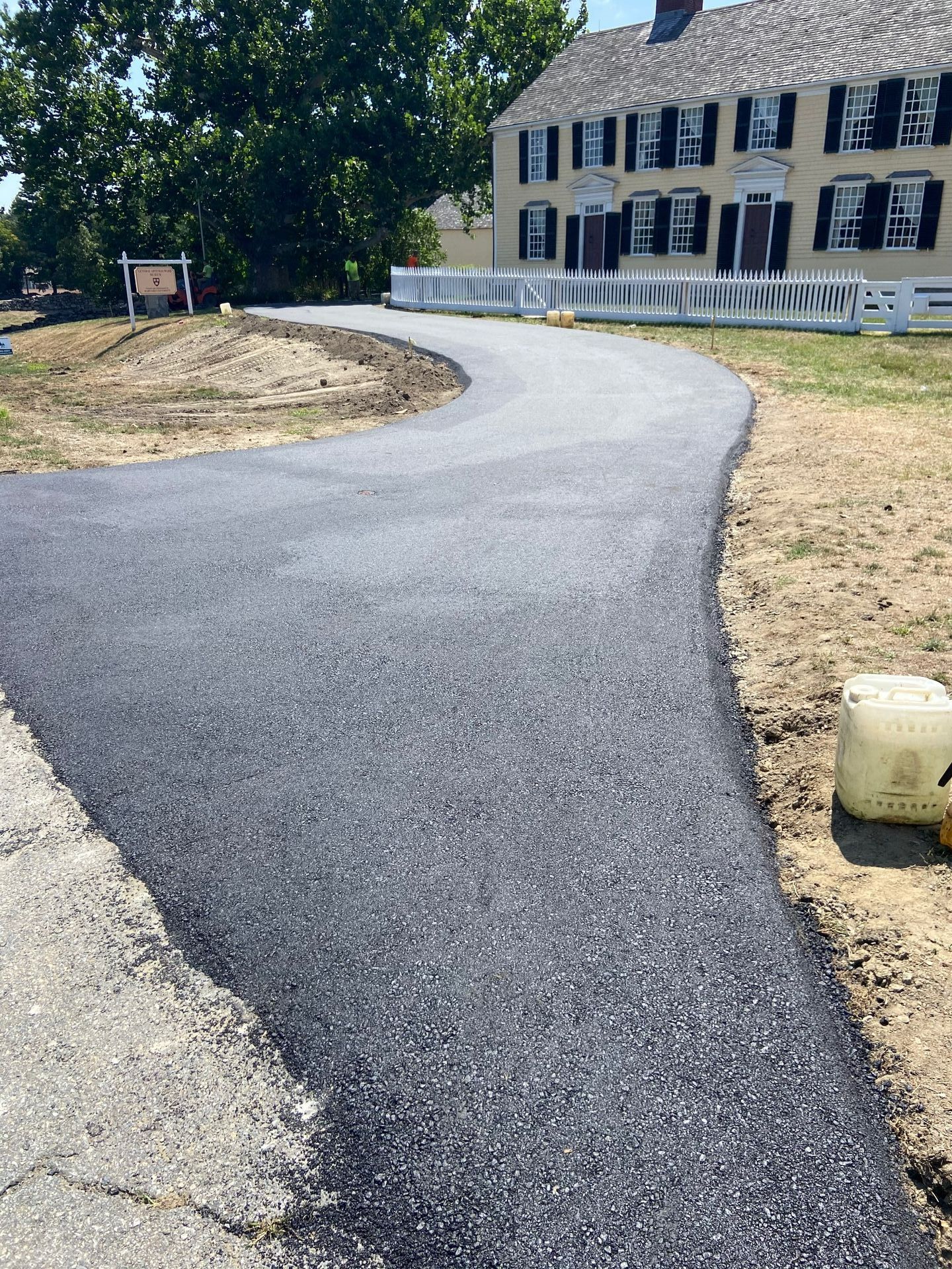 Newly paved asphalt driveway curves towards a light yellow house with black shutters.