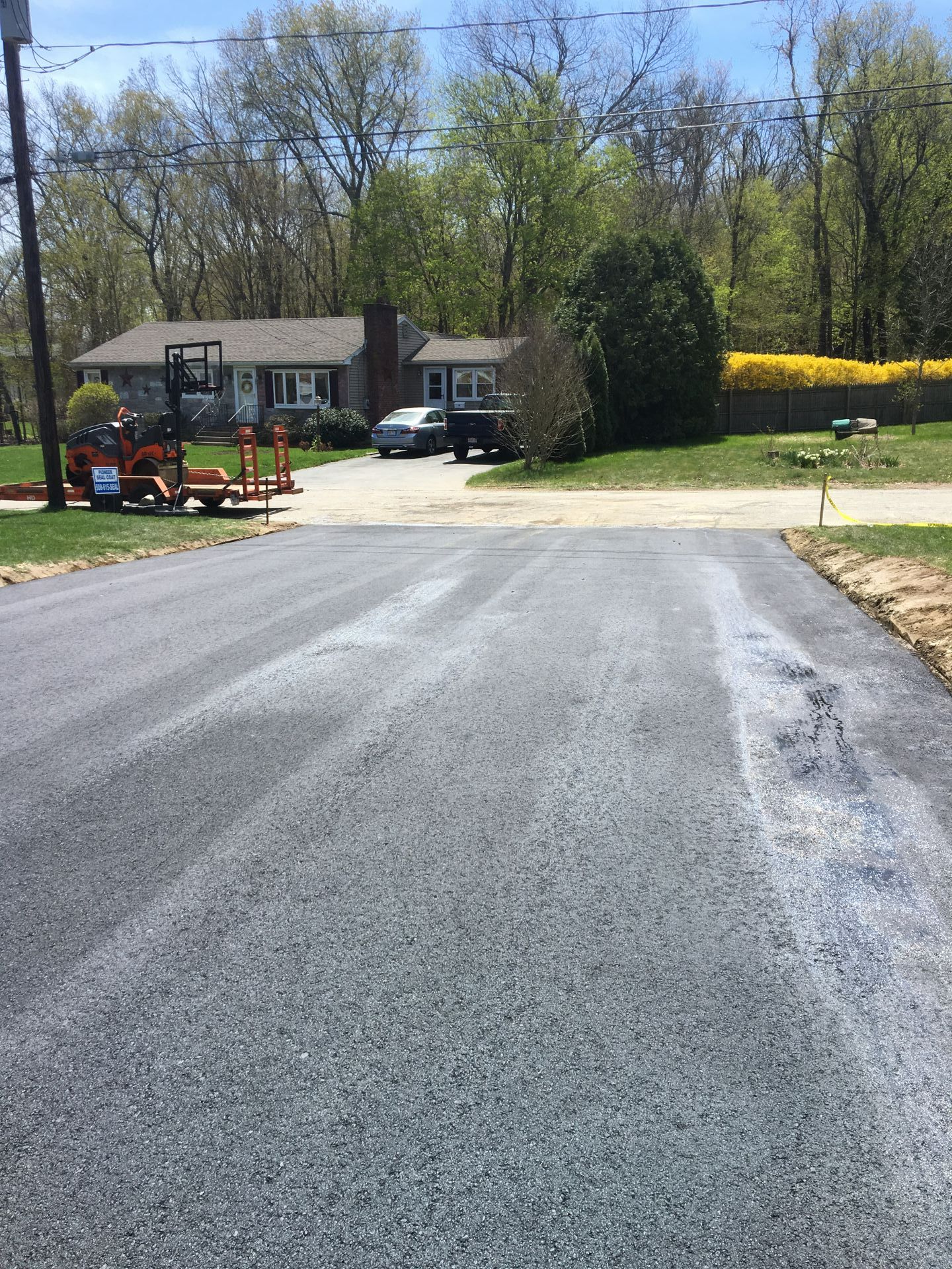 Newly paved asphalt driveway leading to a house, with construction equipment visible on the left.