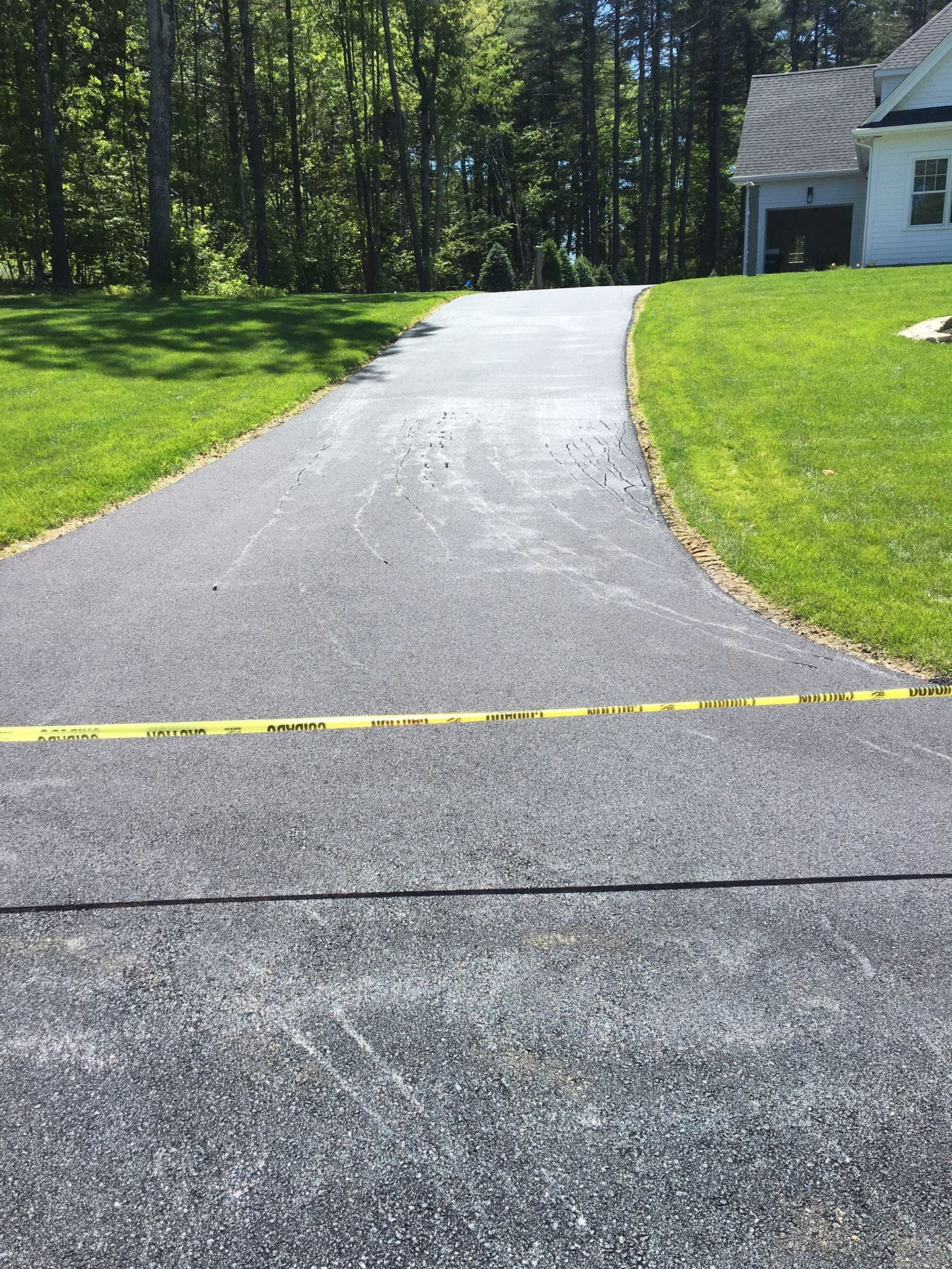 Asphalt driveway curving towards a house, yellow caution tape across it, and green lawn on either side.