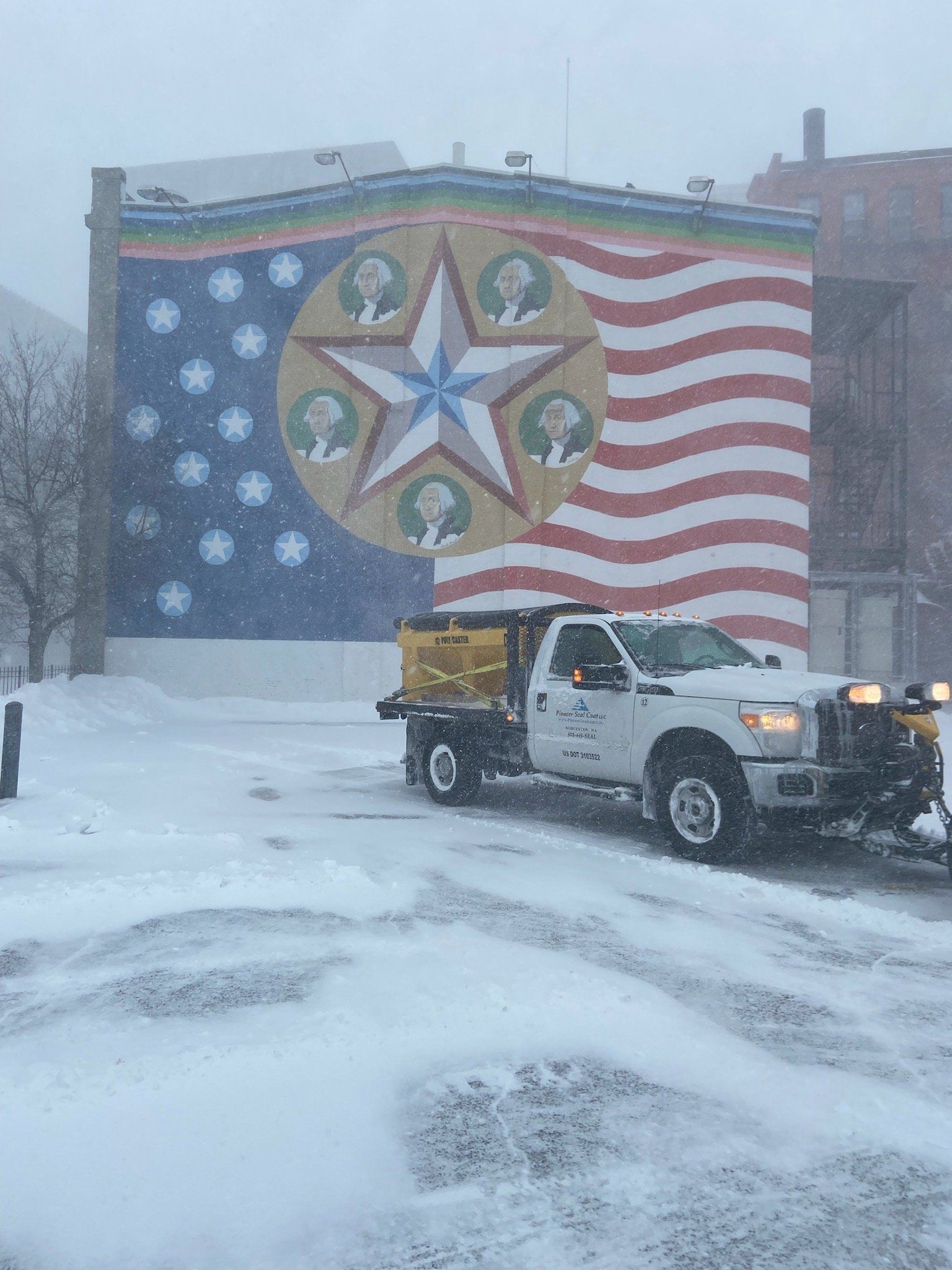 Snowplow clearing snow in front of a colorful American flag mural on a building. Winter scene.