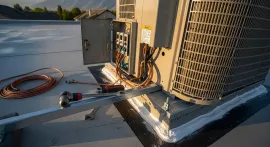 HVAC rooftop unit with coiled copper tubing and tools on a flat roof at sunset