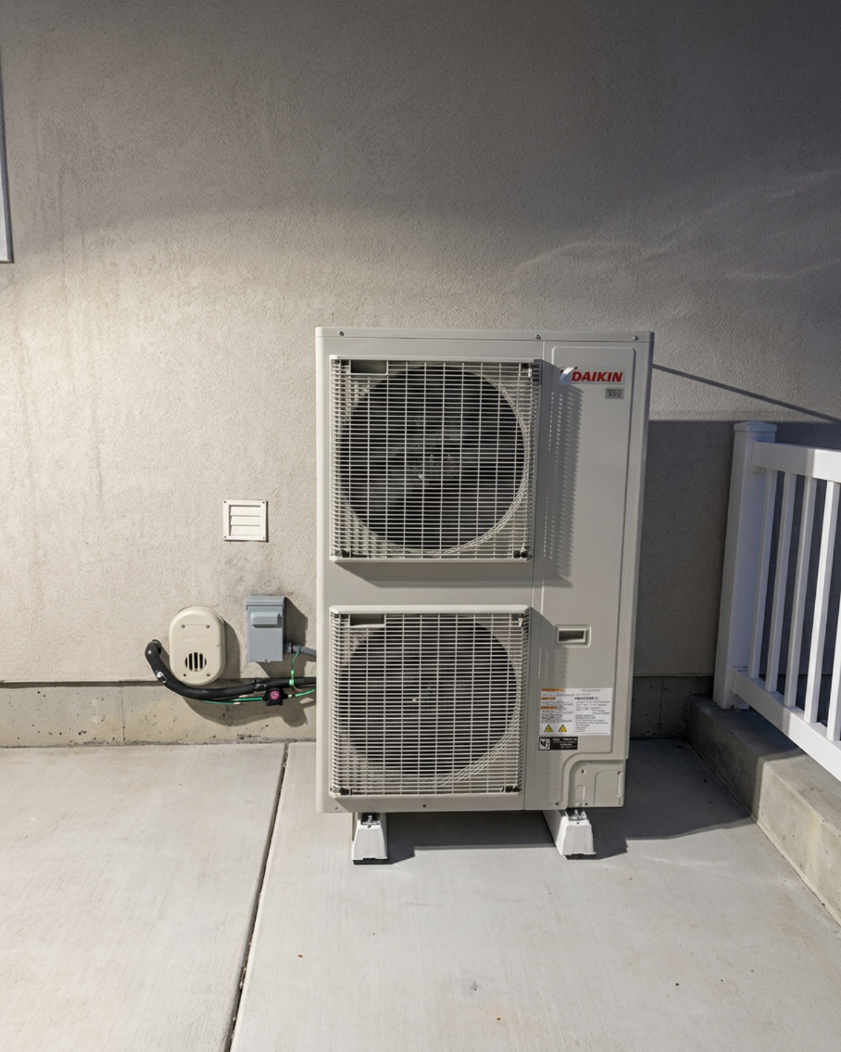 Two stacked outdoor HVAC units against a wall on a concrete rooftop or balcony.