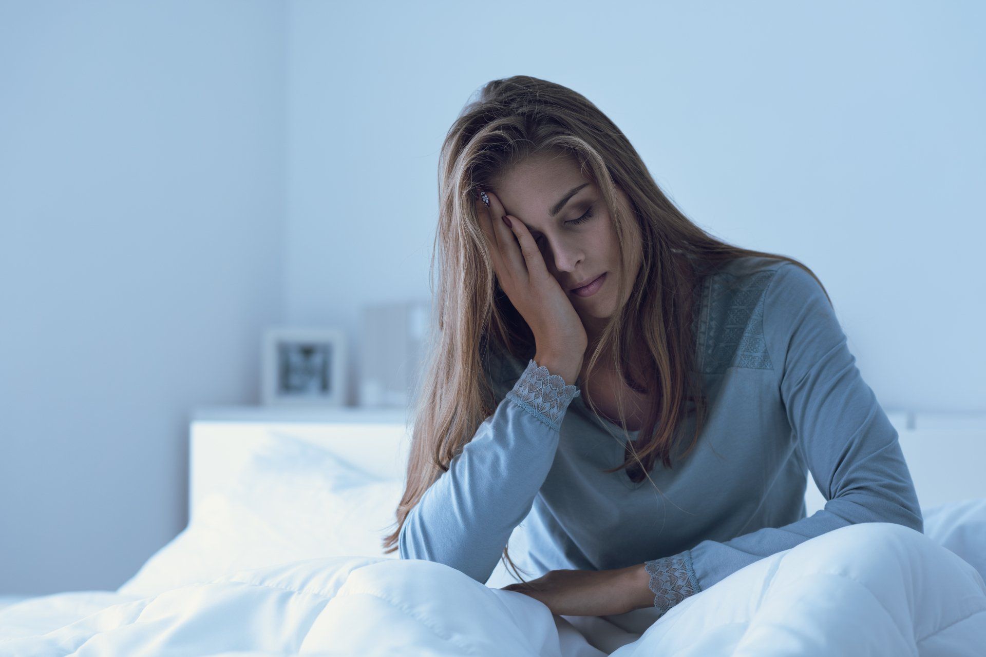 A woman is sitting on a bed with her head in her hands.