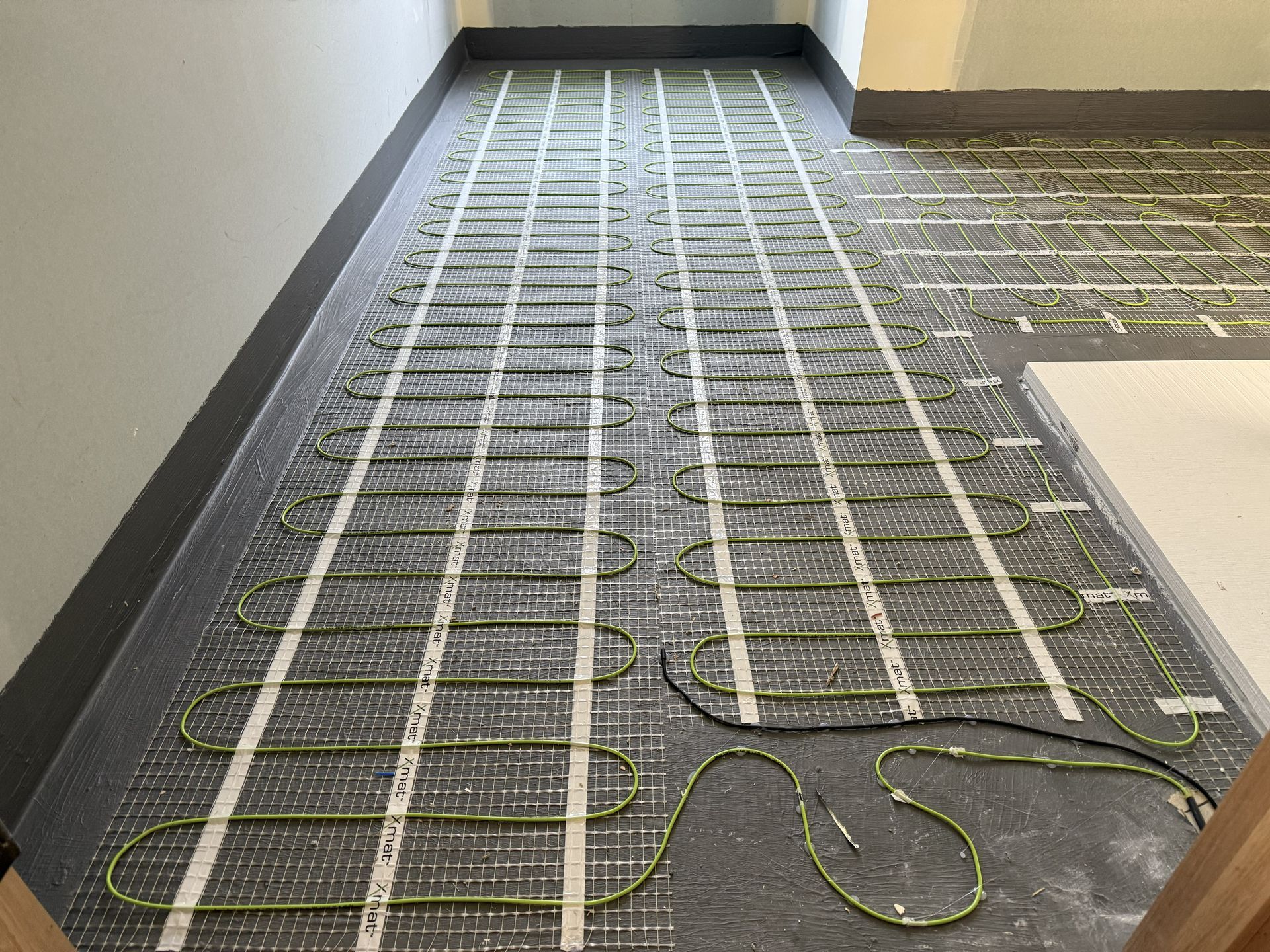 Carpeted floor with white tubing laid in a radiant heating loop pattern during installation