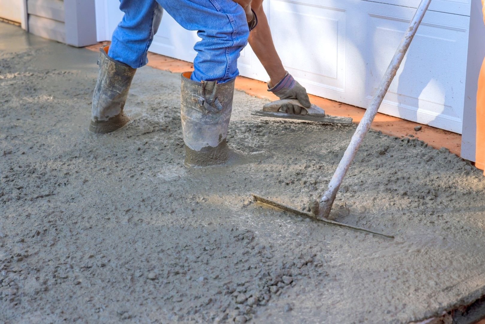 A man is spreading concrete on a sidewalk with a rake.