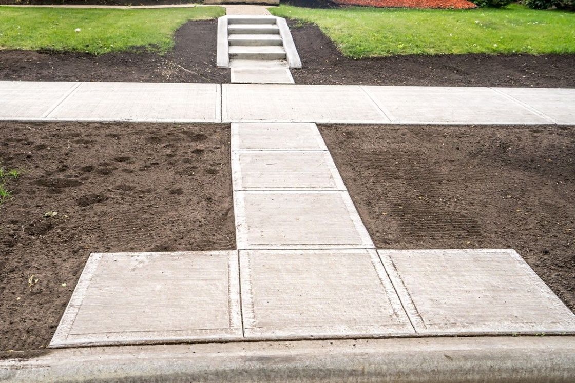 A concrete sidewalk with stairs leading up to a grassy area.