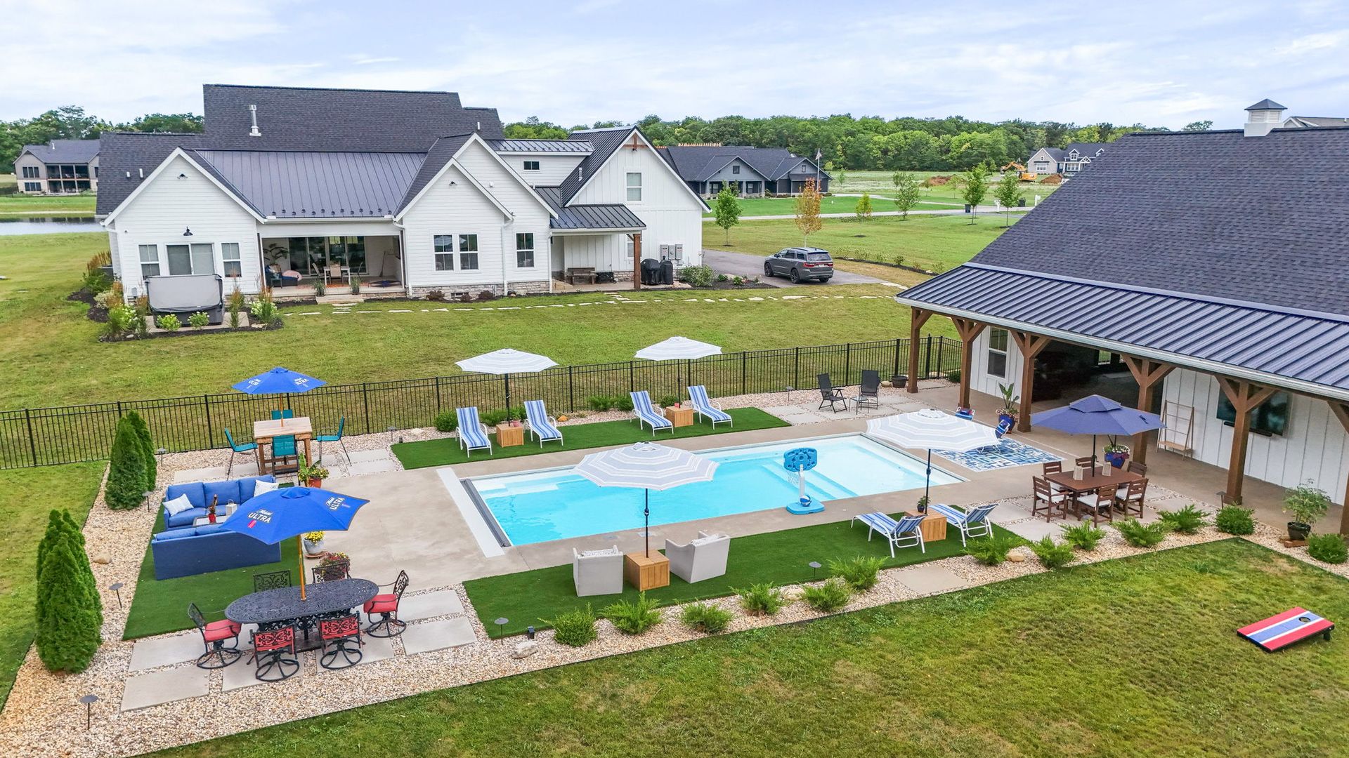 A luxurious backyard with a pool, outdoor kitchen, and a lit fire pit, all set against a dusk sky.