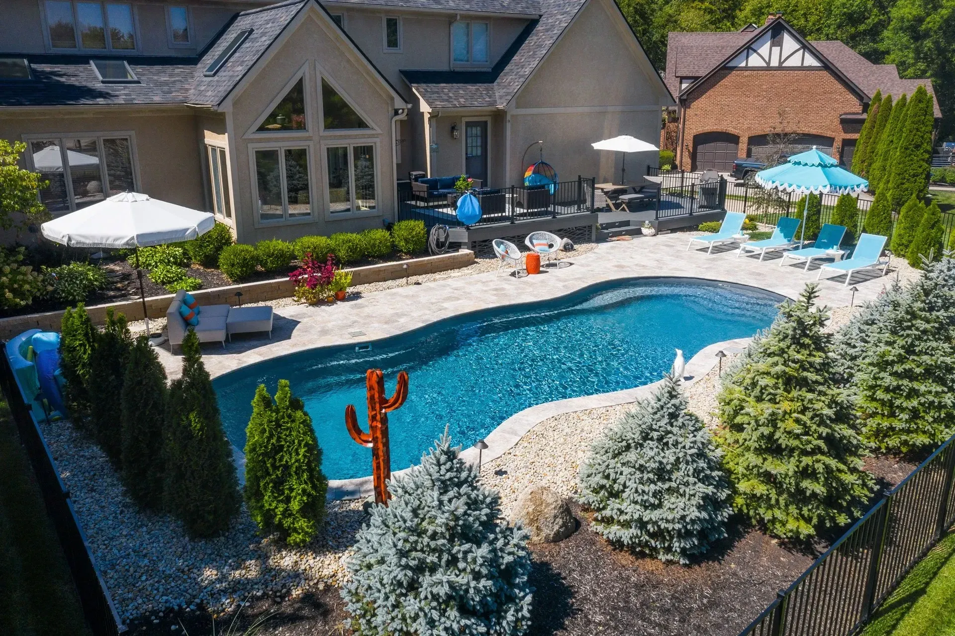 Backyard with a pool, patio, and a house. The pool has a unique shape with lounge chairs, and some decorations like a cactus statue.