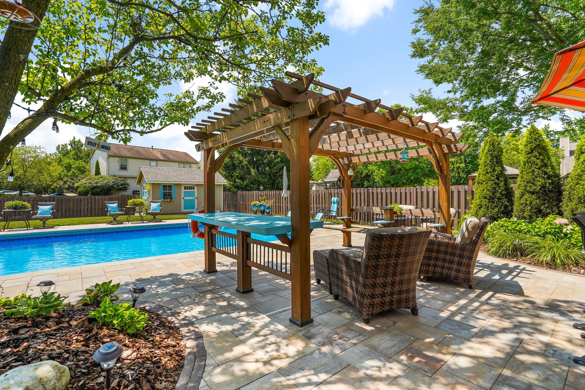 Outdoor swimming pool on a patio with lounge chairs and tropical plants.