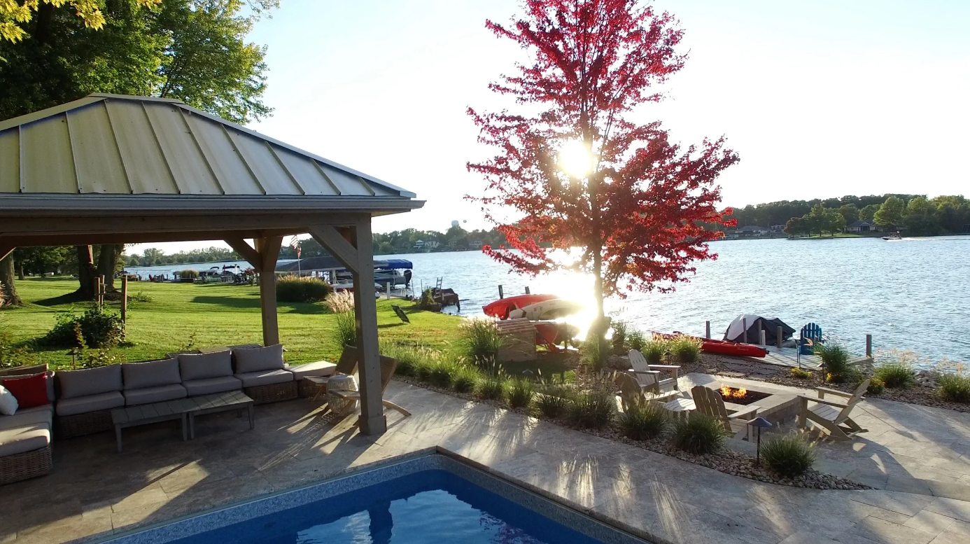 Scenic gazebo and patio by the lake, surrounded by lush landscaping near a pool.