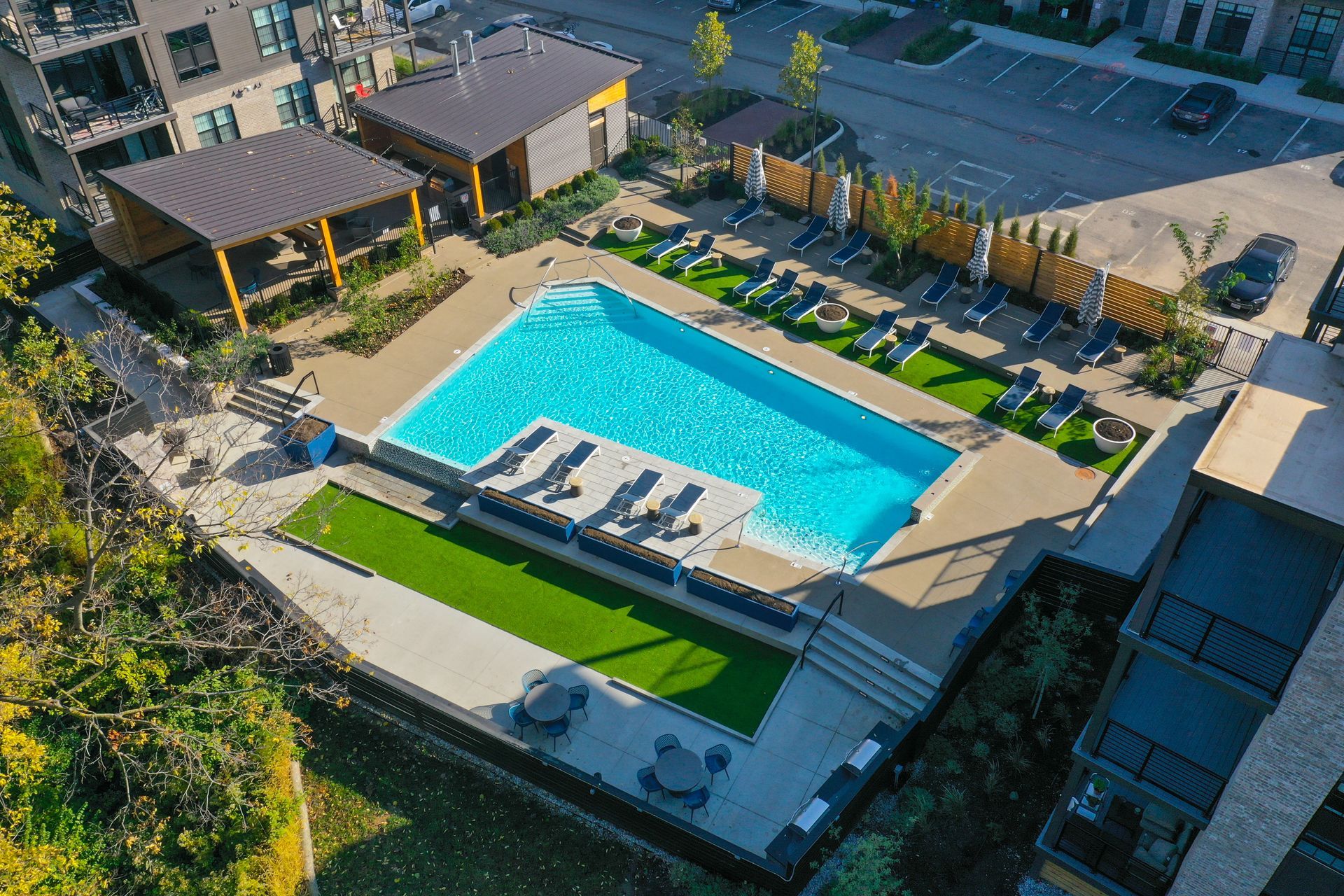 Aerial view of an apartment complex pool with lounge chairs, artificial grass, and a covered seating area.