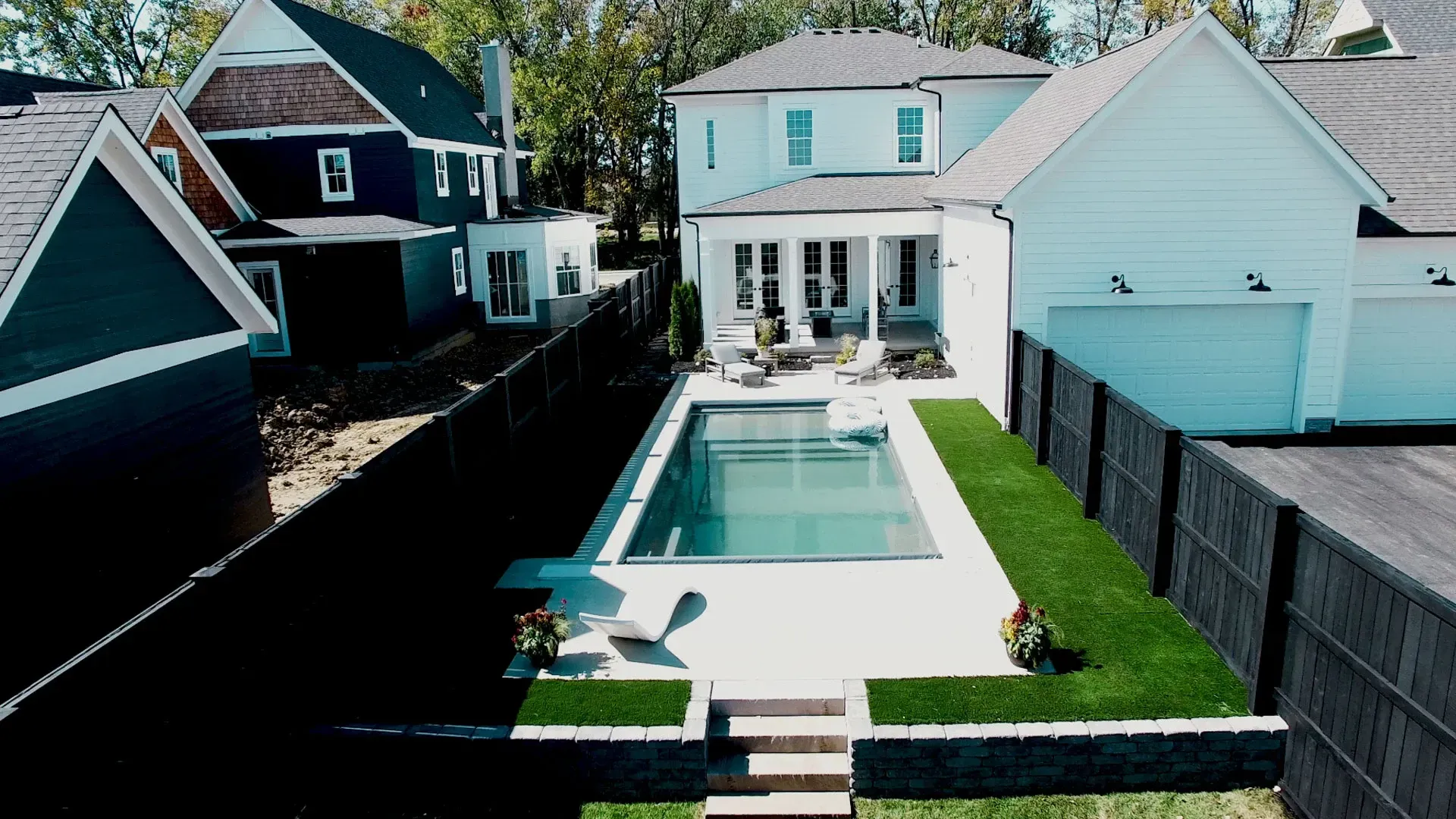 Backyard with a pool, patio furniture, and a white house. Green turf lines the pool area.