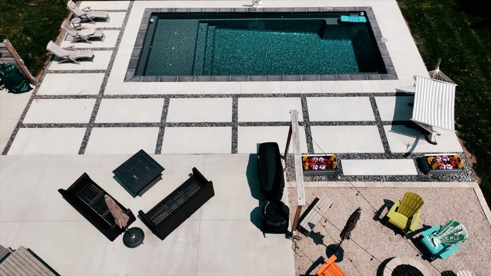 High-angle view of a backyard with a pool and patio. Features include a rectangular pool, seating areas, and a fire pit.