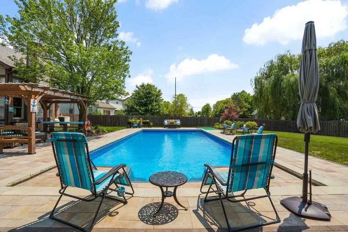 Two blue striped chairs face a pool on a sunny day; a small table and closed umbrella are nearby.