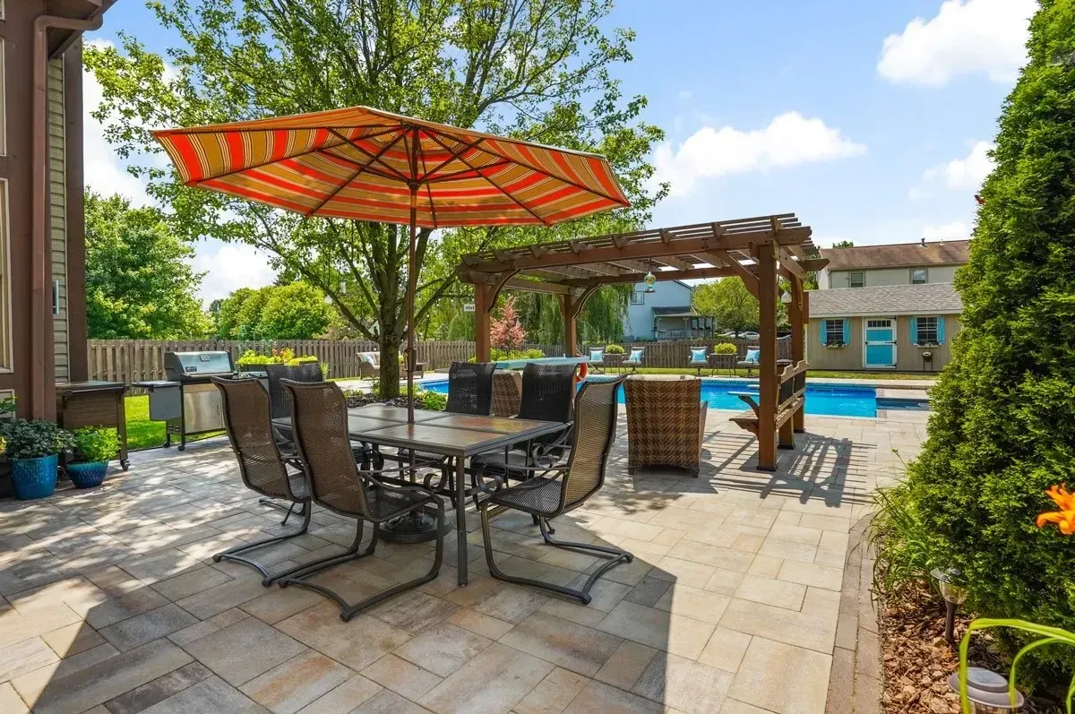 Patio with a dining set under an umbrella, grill, and pool in the background.