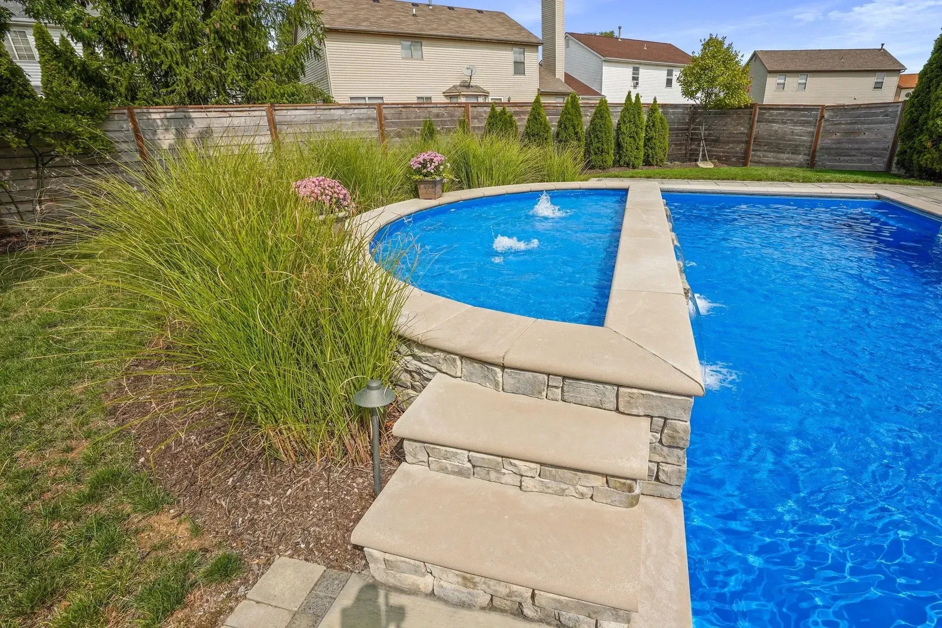A large swimming pool with stairs leading to it in a backyard.