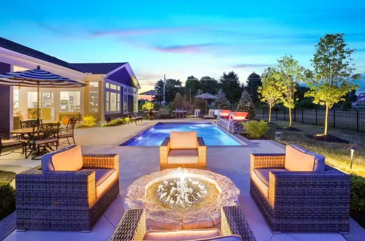 A backyard oasis featuring a fire pit, swimming pool, lounge chairs, and lush garden
