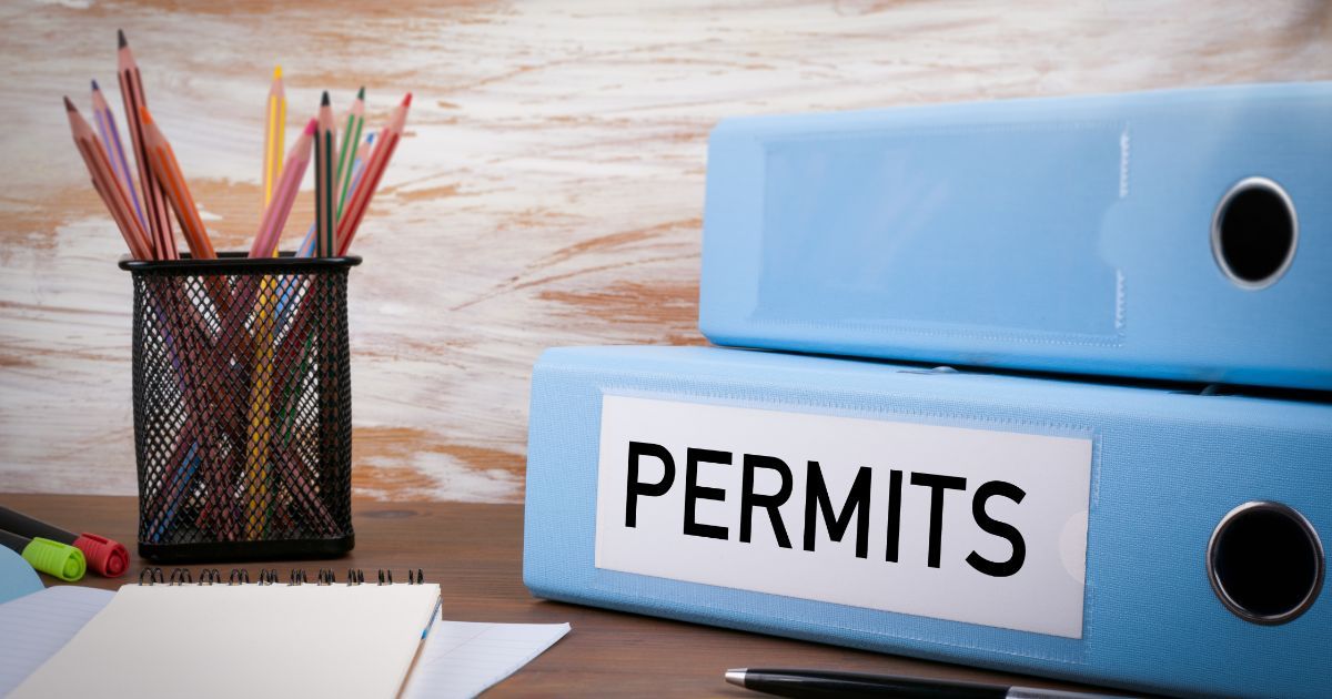 Desk arrangement featuring small business permits, licenses, notes, colored pencils, and a permit organizer.