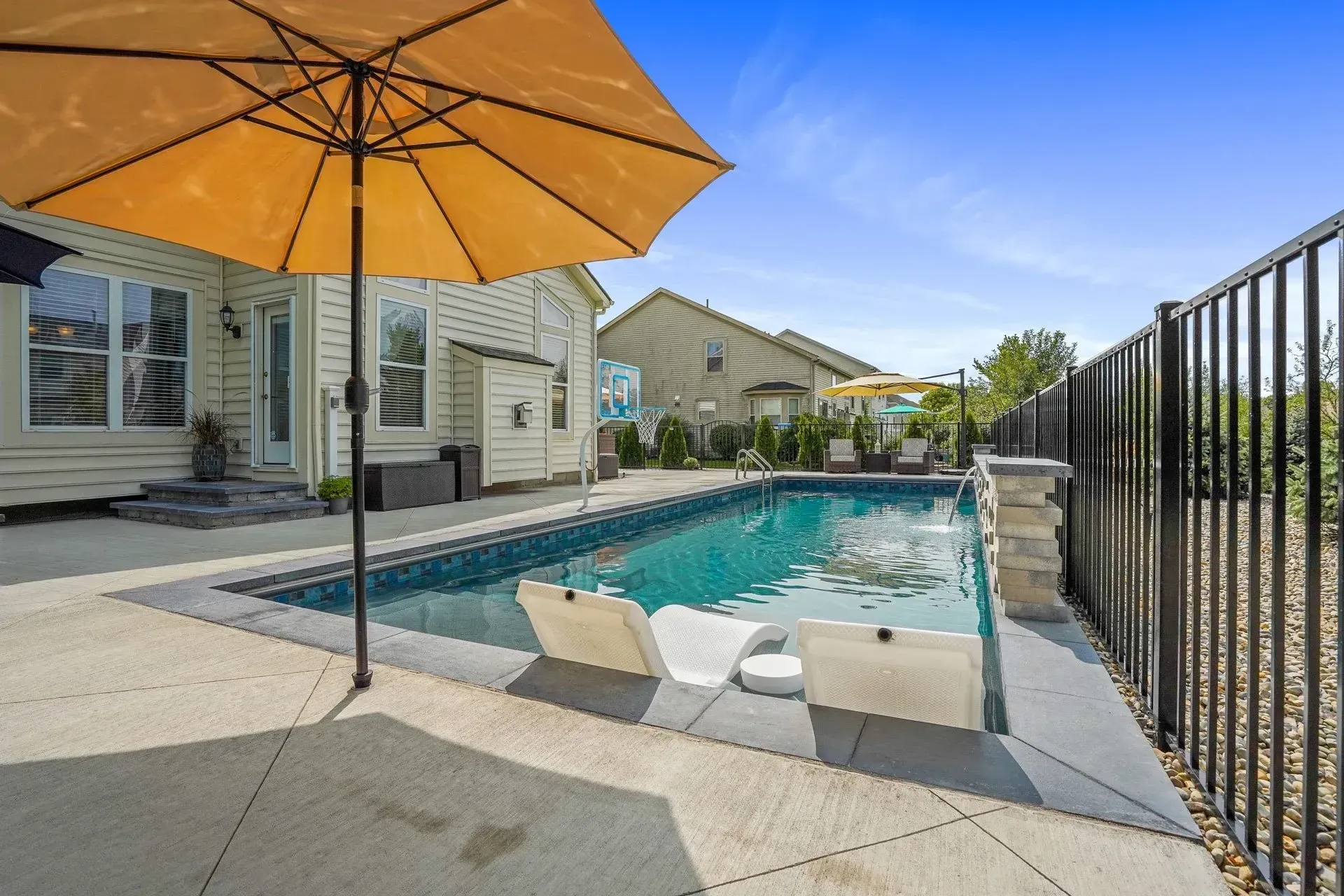 Backyard with rectangular pool, two lounge chairs, and a yellow umbrella; fence and house visible.