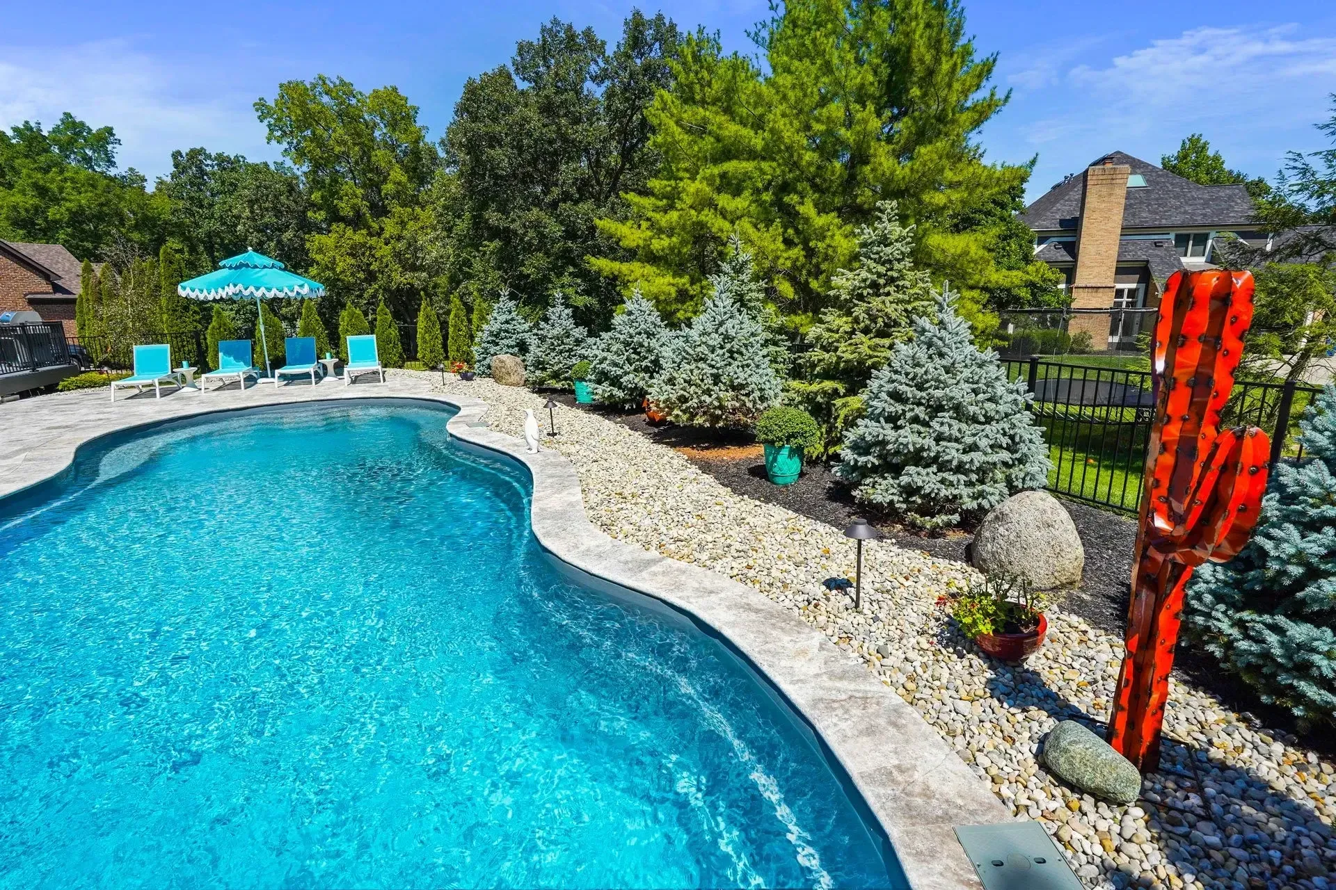 A backyard pool area with a turquoise striped umbrella, lounge chairs, and lush landscaping.