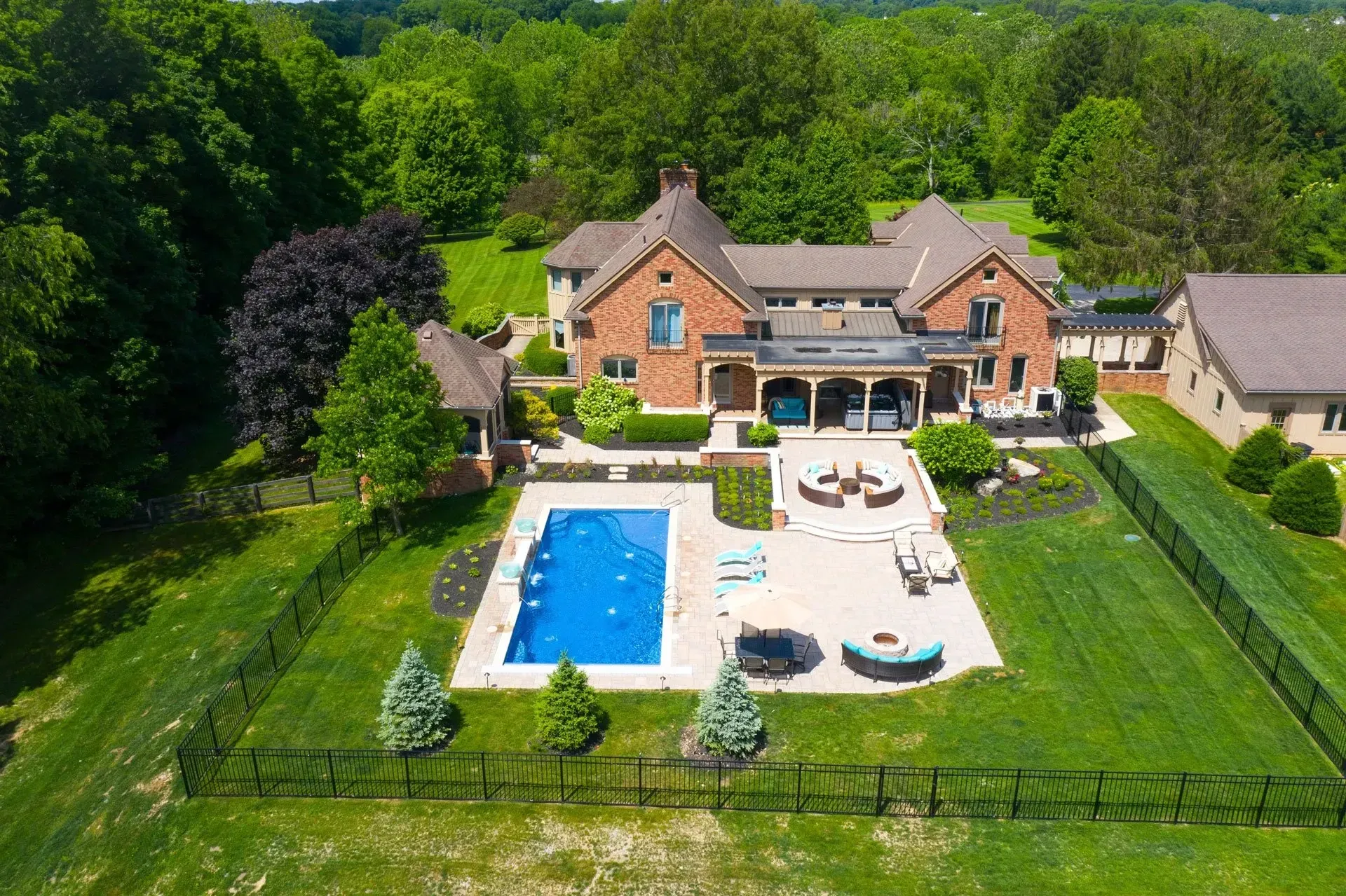 Aerial view of a large brick house with a pool and patio surrounded by green lawn and trees.