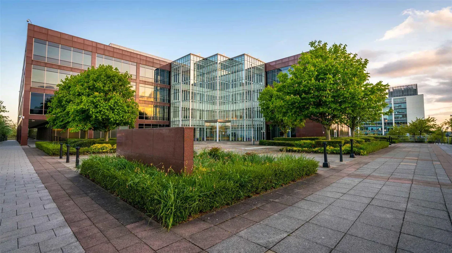 Modern office building with glass and brick facade, featuring landscaping and a paved plaza under a clear sky.