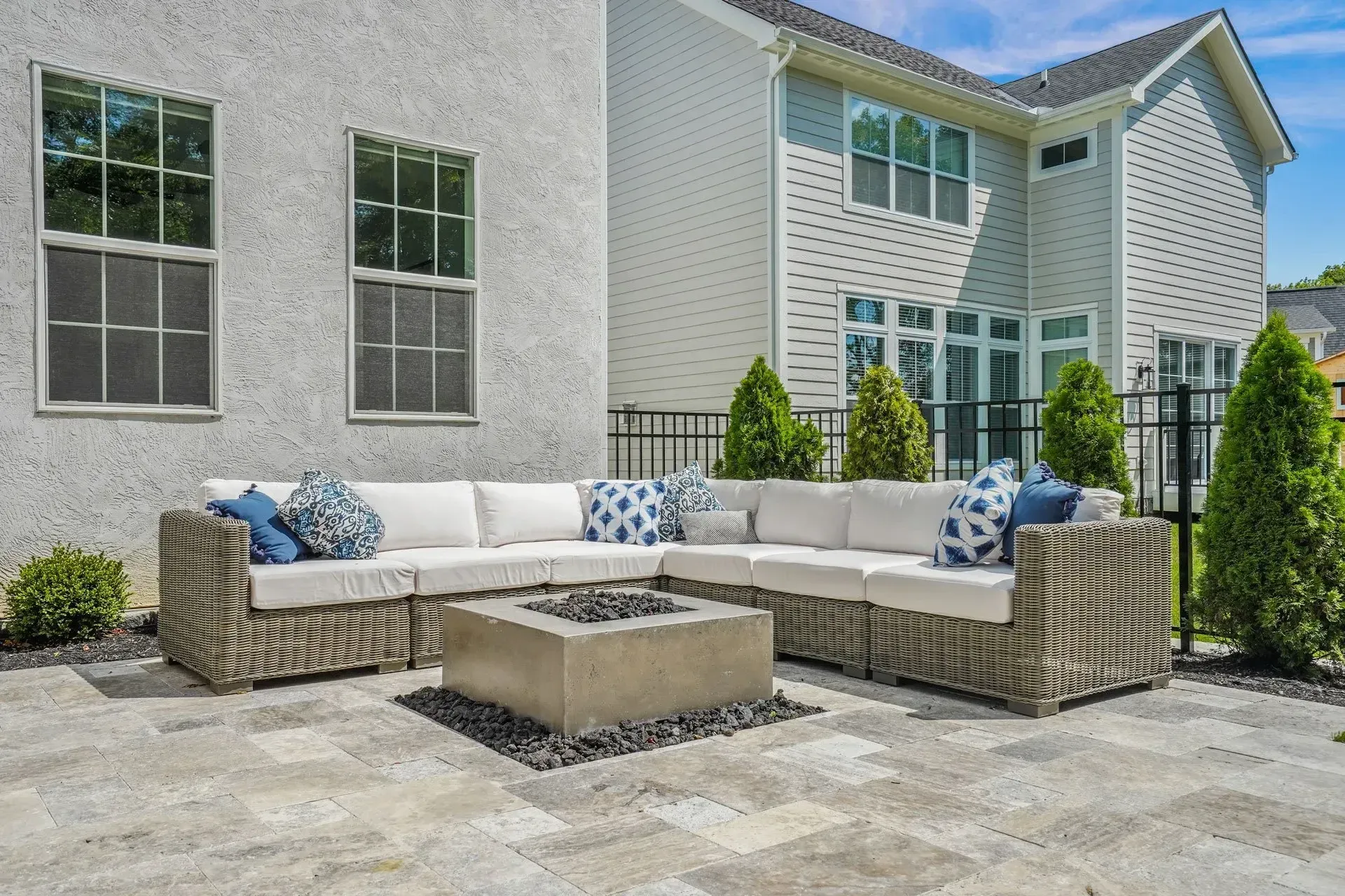 Outdoor patio with a gray sectional sofa, fire pit, and a two-story house in the background.