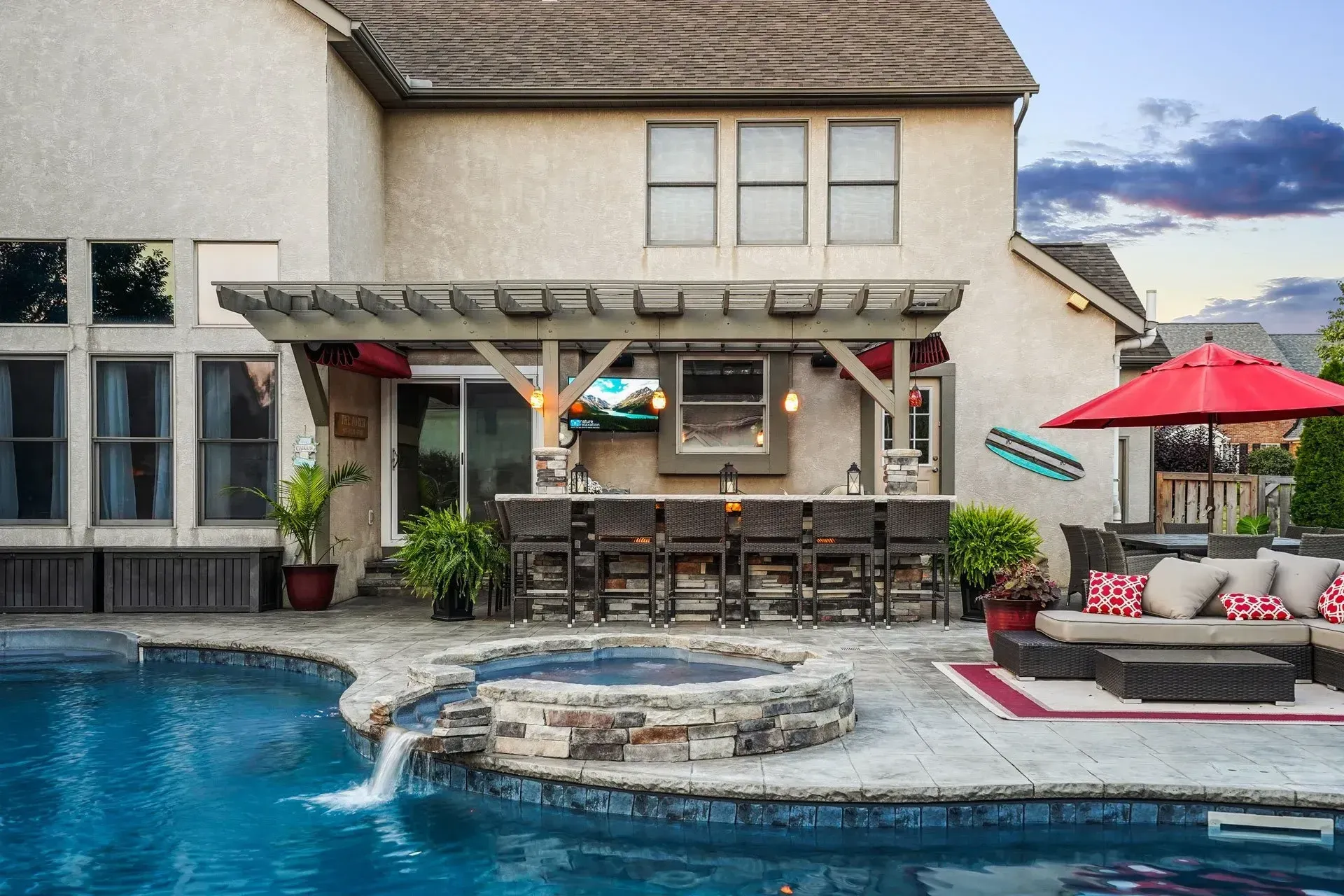 Backyard with a pool, outdoor bar with stools, and a seating area under a red umbrella.