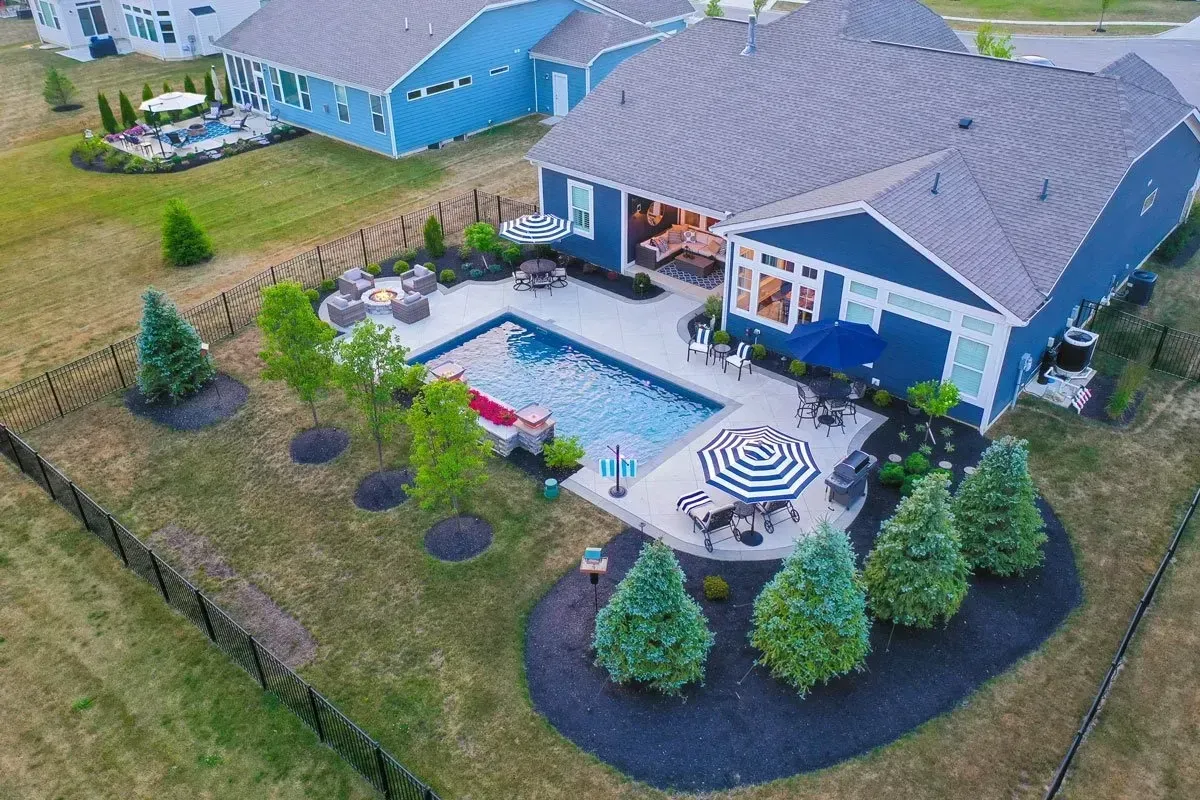 An aerial view of a blue house with a pool in the backyard. The backyard features a patio, fire pit, and landscaping.