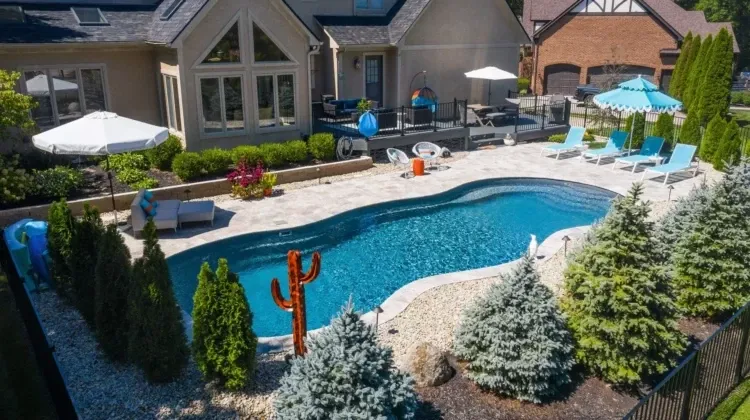 Aerial view of a backyard with a kidney-shaped pool. Blue lounge chairs surround the pool, with trees and landscaping.