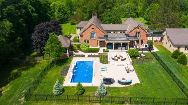Aerial view of a large brick home with a pool and patio, surrounded by green lawn and trees.