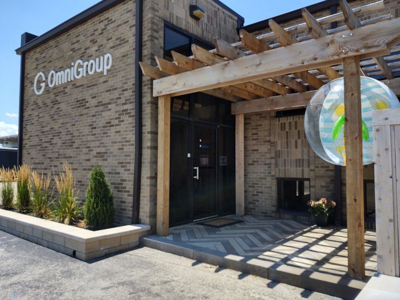 The exterior of OmniGroup's building with a wooden pergola over the entrance. Beige brick facade, with a large beach ball decoration.