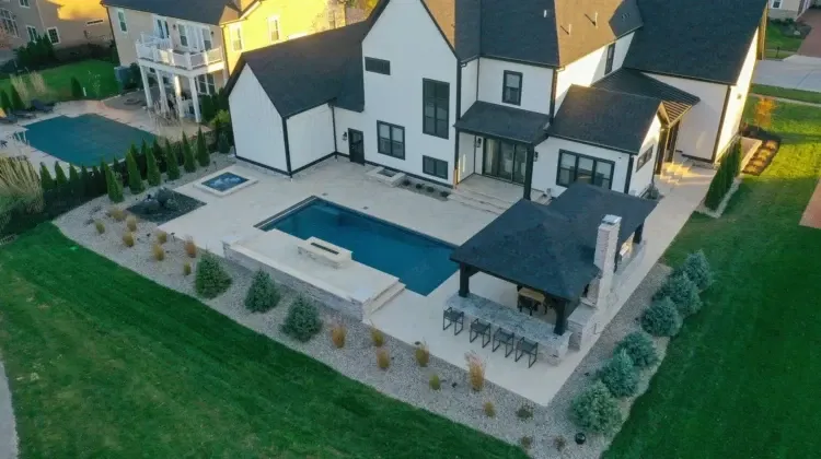 Aerial view of a modern white house with black trim, a pool, and a gazebo on a large lawn.