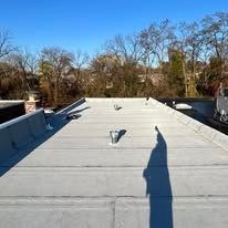 Flat rooftop with white membrane, vents, and a long shadow under a clear blue sky.