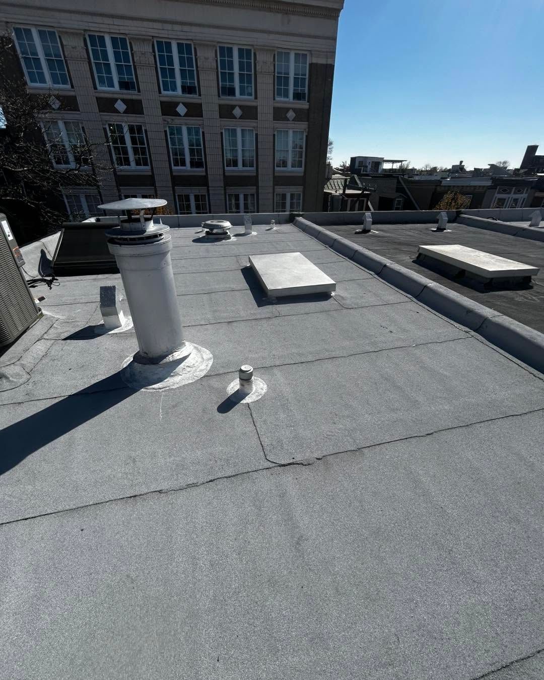 Rooftop with gray gravel, white vents, and low skylights under a clear blue sky.