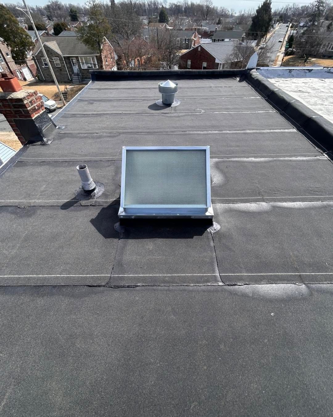 Flat rooftop with gravel, vents, and a skylight overlooking houses in the distance.