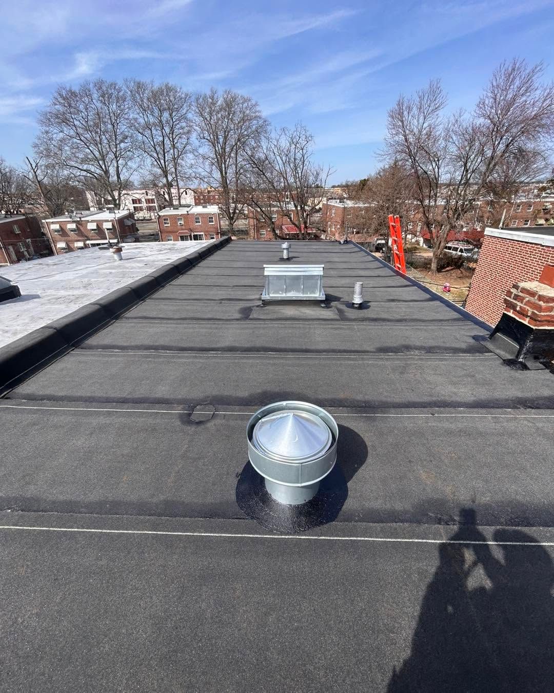 Flat black rooftop with vents and a snowy edge under a blue sky