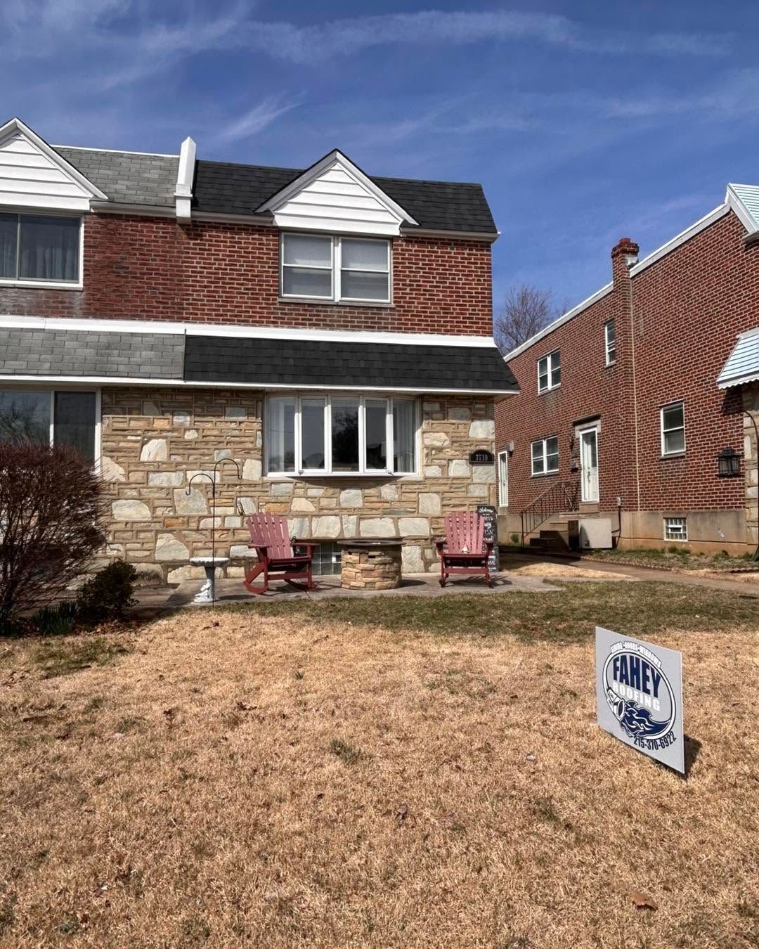 Brick-and-stone townhouse with front lawn and a real estate sign under a blue sky