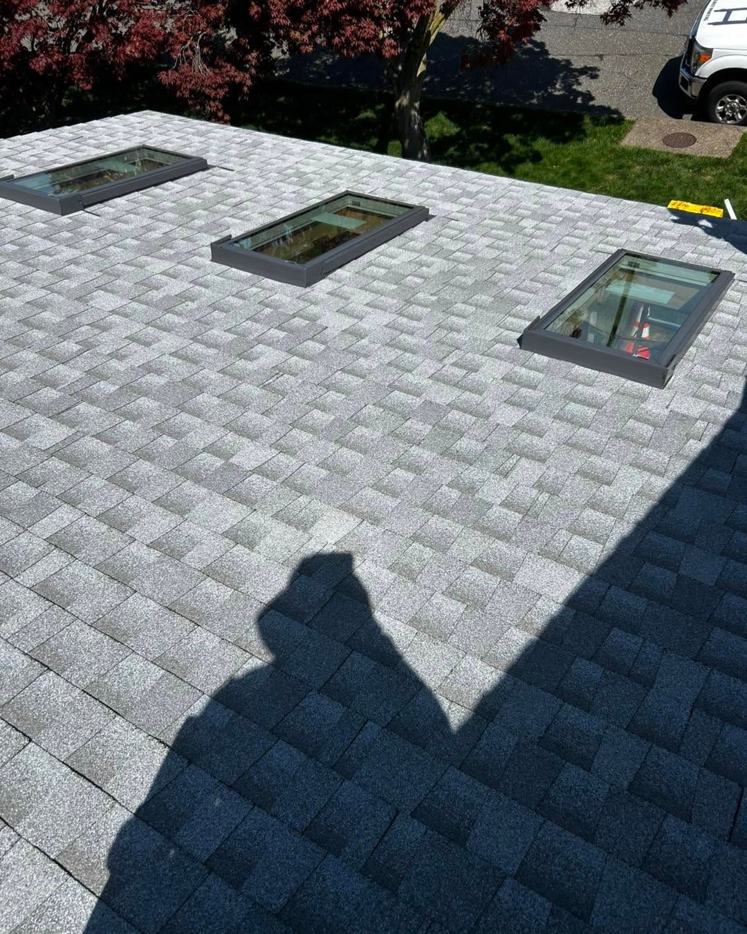 Gray shingle roof with three skylights, seen from above with tree shadows and a patch of garden nearby