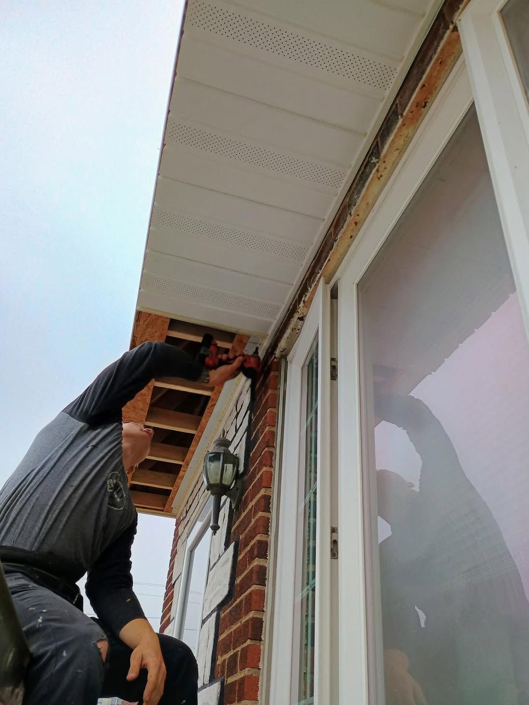 Person working on the exterior roofline of a brick house near a window and soffit