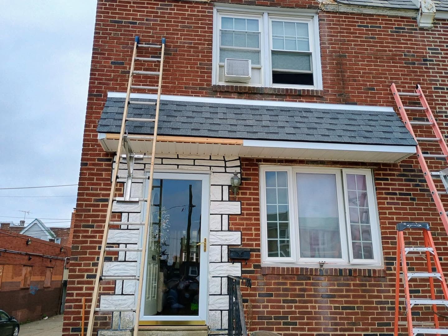 Brick house facade with ladders, a glass front door, and an open second-floor window under repair