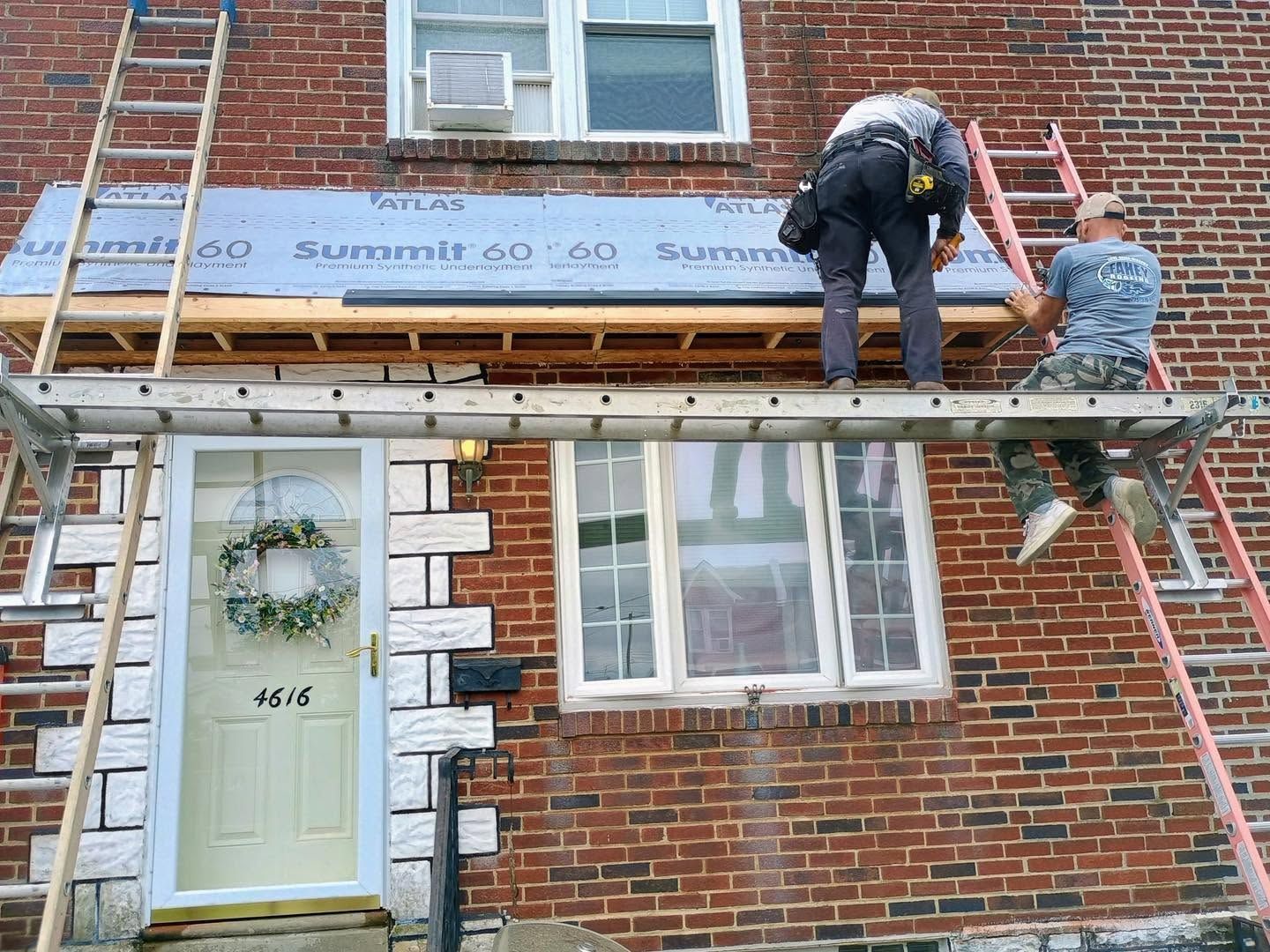 Two workers installing siding on a brick house exterior scaffold