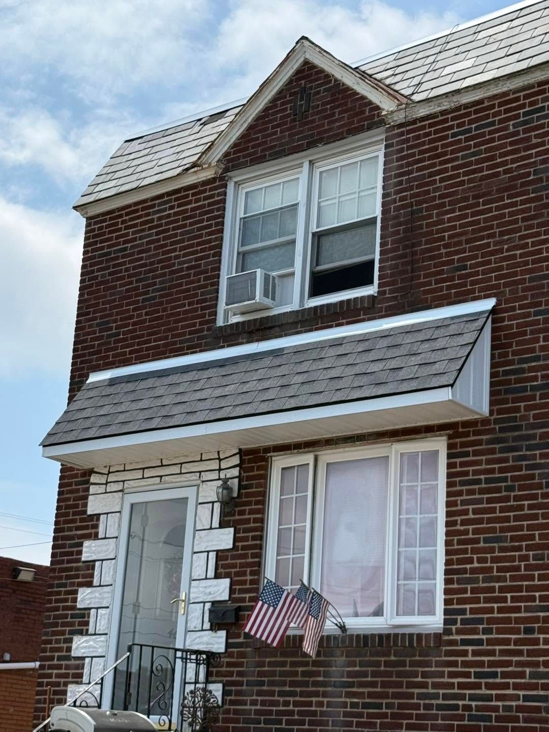 Brick townhouse with a white awning, upstairs windows, and a small American flag by the front door