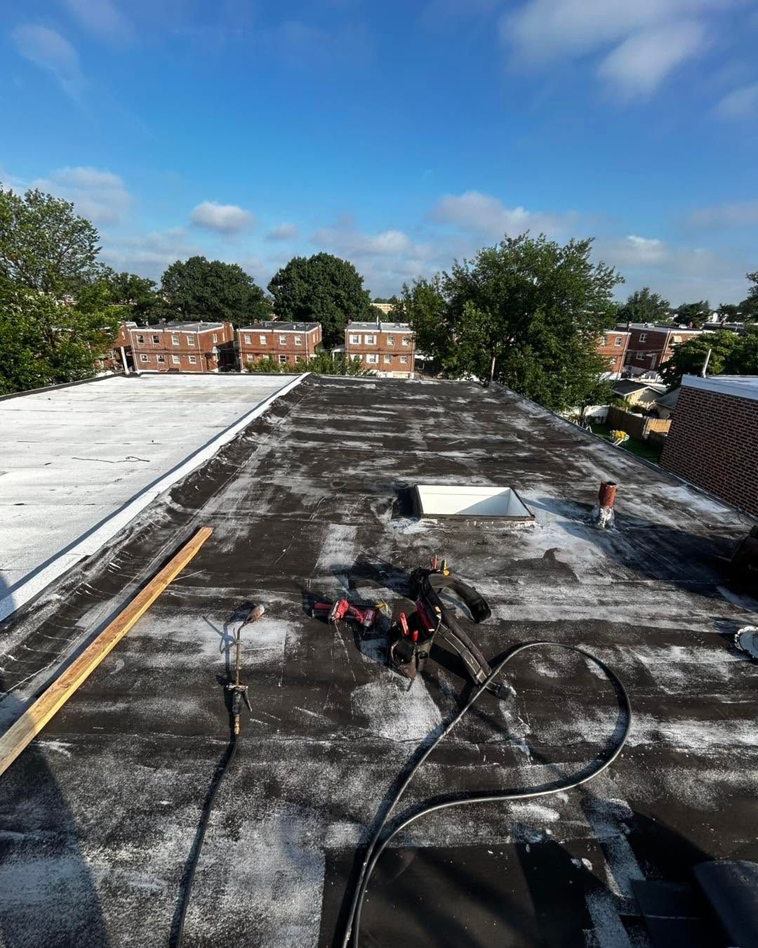 Rooftop with roofing tools, white membrane, and city buildings under a blue sky