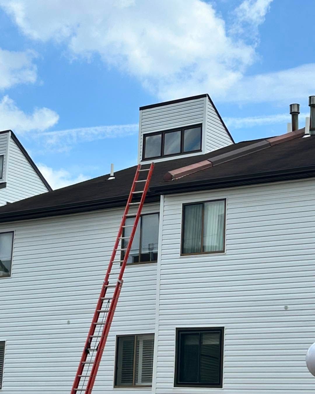 Red ladder leaning against a white house roof under a blue sky.