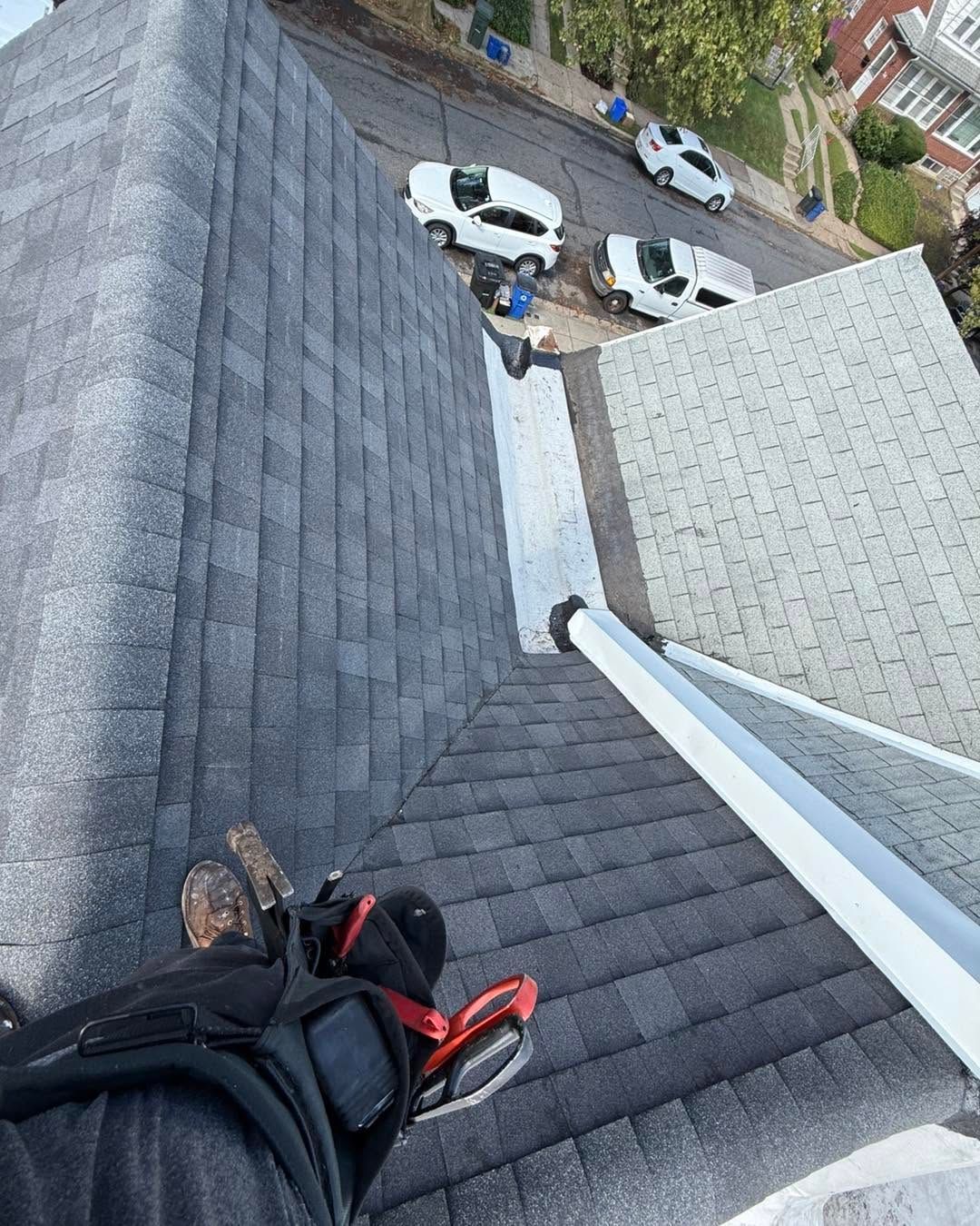 Person on a steep gray shingled roof above parked white cars below