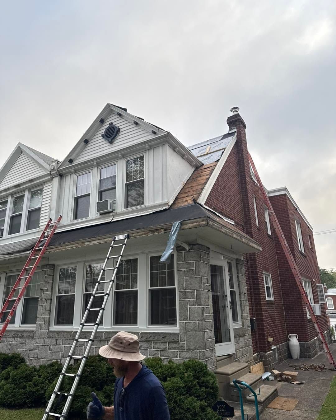 Workers on ladders painting a gray and red house exterior with stone and white trim.