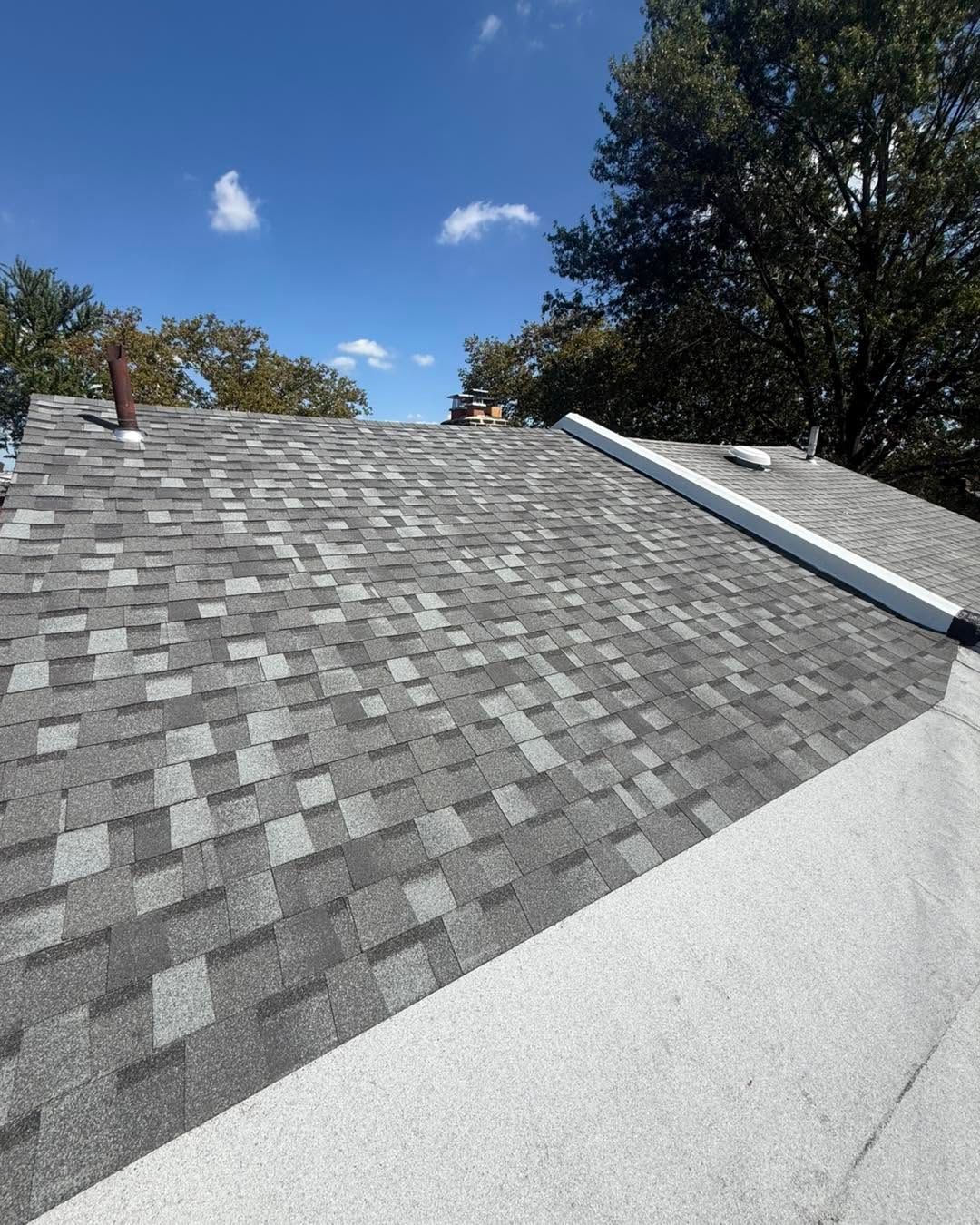 Gray shingled roof with white trim under a blue sky and trees
