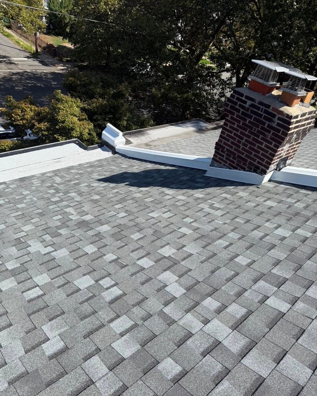 Roof shingles with a brick chimney and trees in the background